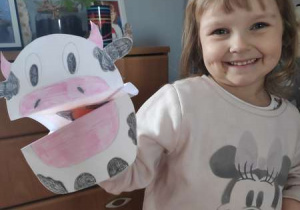 Uśmiechnięta dziewczynka trzyma zrobioną z papieru krowę z zamkniętą mordką